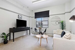 A modern living room with a flat-screen TV, a black console table, a round coffee table, a sofa, and a dining area with chairs.