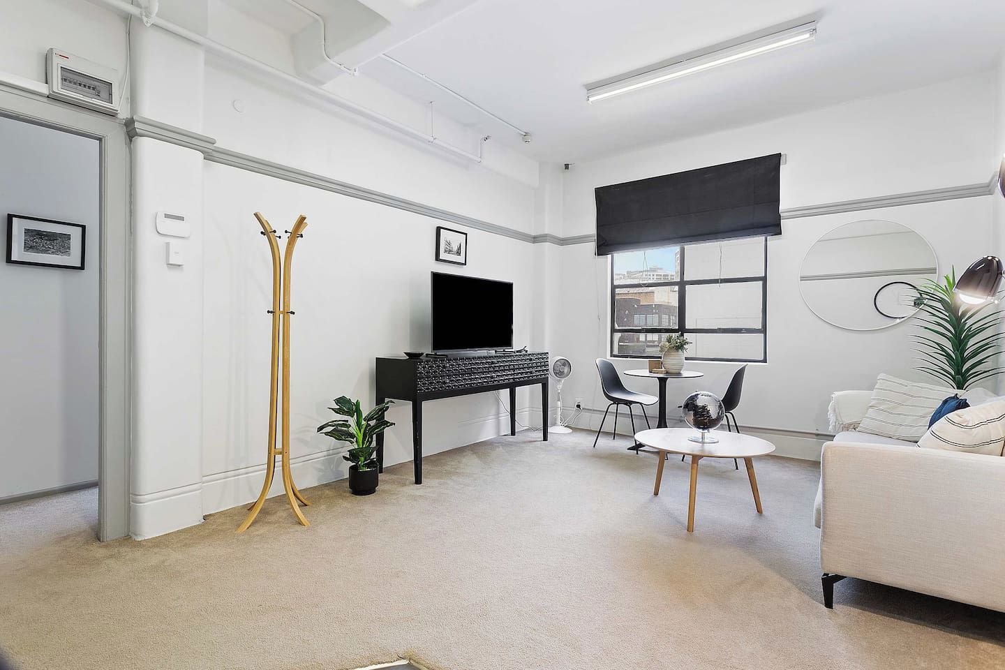 A modern living room with a flat-screen TV, a dining table, chairs, a sofa, and a large window with blinds.
