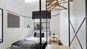 A modern bedroom with a bed, a wooden table, a hanging clothes rack, and a wall-mounted artwork.
