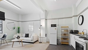 A modern kitchen with white appliances, a dining area with a white table and chairs, and a living room with a sofa and a coffee table.