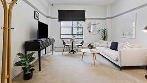 A modern living room with a sofa, a coffee table, a TV, a piano, a dining table with chairs, and a potted plant.