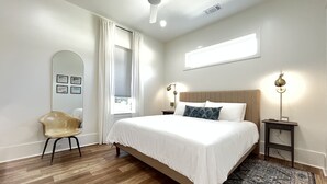 Un dormitorio con cama, una silla, una mesita de noche, una lámpara de pie y un ventilador de techo.
