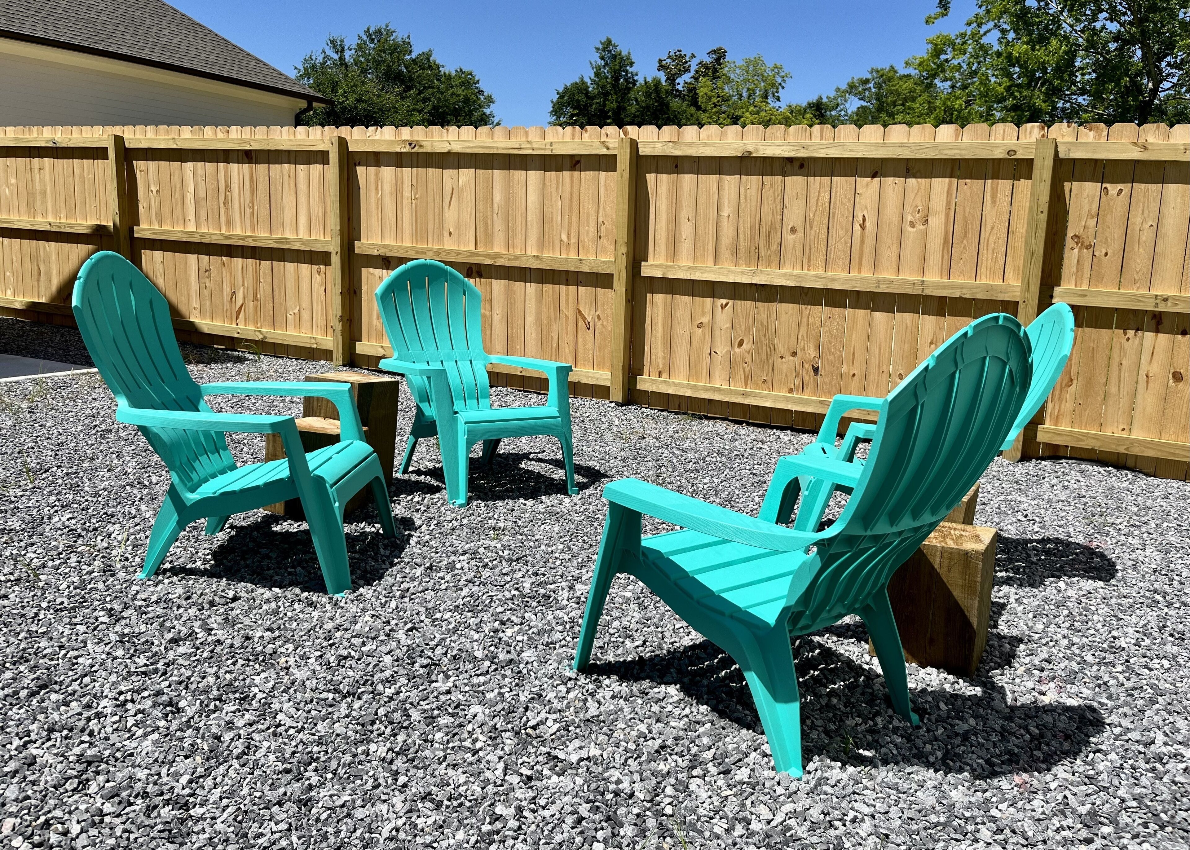 Drie turquoise Adirondack stoelen staan op grind, met een houten omheining op de achtergrond.