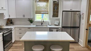 Una cocina moderna con armarios blancos, un refrigerador de acero inoxidable y dos taburetes de bar.