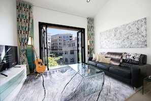 Un salon moderne avec une table basse en verre, un canapé noir, une guitare et un téléviseur posé sur un meuble.