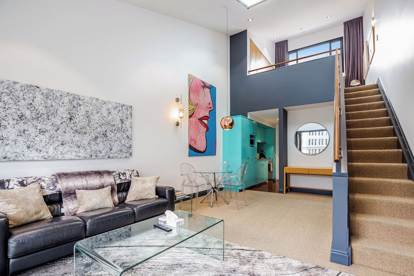 A modern living room with a sofa, coffee table, and artwork. A staircase leads to an upper level.