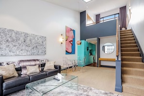 Un salon moderne avec un canapé, une table basse et des œuvres d’art. Un escalier mène  à un niveau supérieur.