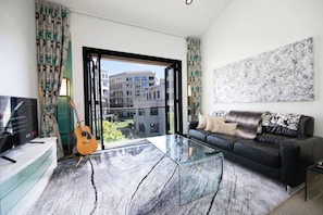 Ein modernes Wohnzimmer mit einem Glastisch, einem schwarzen Ledersofa, einer Gitarre und einem Fernseher auf einem Schrank.