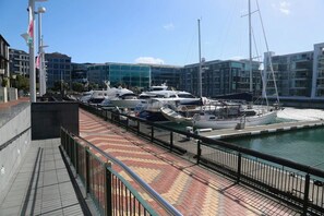 Un puerto deportivo con varios yates amarrados, un paseo peatonal y edificios modernos al fondo.