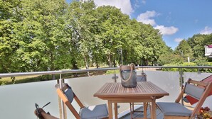 Una terraza con mesa y sillas, barandilla de metal y vista a árboles.