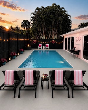 A pool area with lounge chairs, a table, and a fence with string lights.