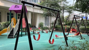 Children can play on swings, a slide, and a climbing structure in this outdoor playground.