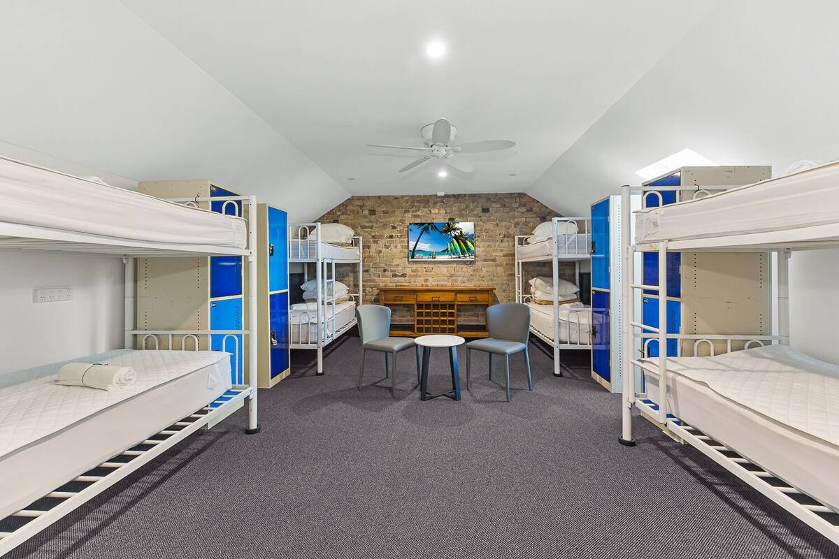 A dormitory room with bunk beds, a desk, chairs, and a fireplace.