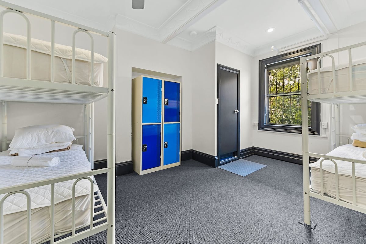 A dormitory room with bunk beds, a wardrobe, a door, and a window.
