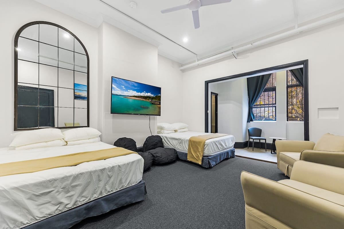 A hotel room with two beds, a TV, a large window, and a seating area.