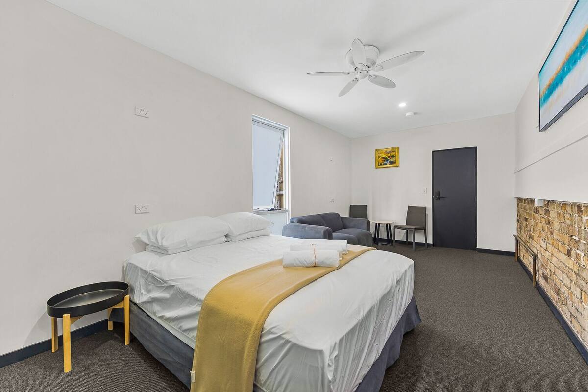 A hotel room with a bed, a desk, a chair, a ceiling fan, and a window.