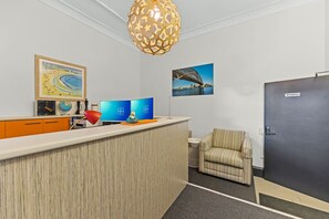 A reception area with a wooden reception desk, two monitors, a globe, a chess piece, and a red lamp. There is a striped armchair and a door labeled "Reception". - London Plane Backpackers - Hostel (Potts Point)