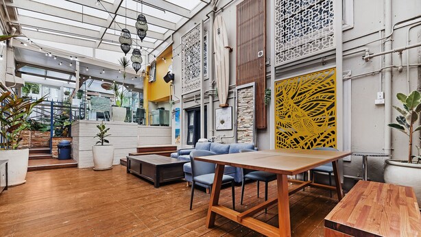 A spacious indoor area with wooden flooring, a blue sofa, a wooden table, and decorative elements like hanging lanterns and patterned screens. - London Plane Backpackers - Hostel (Potts Point)
