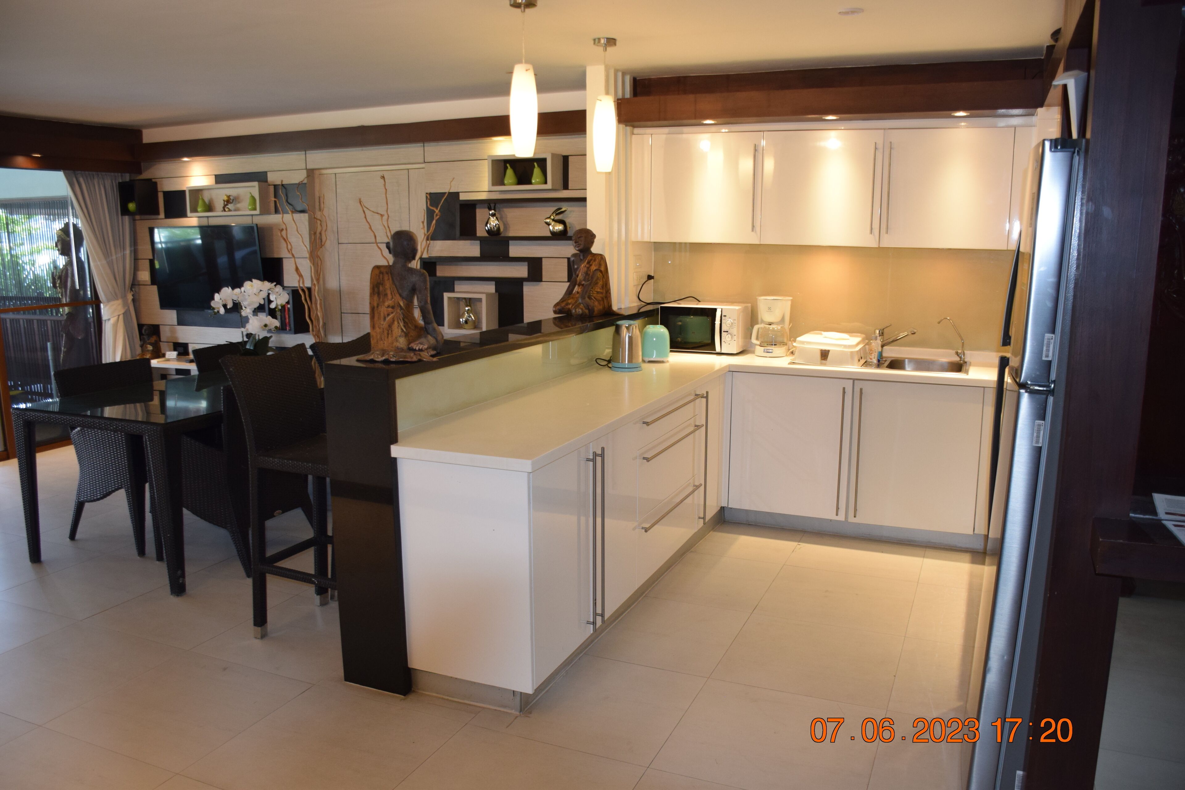 A modern kitchen with white cabinets, a central island, a dining area with chairs, and a refrigerator.