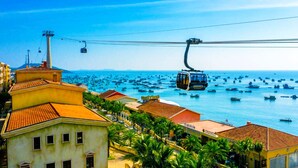 Uma vila costeira com um sistema de teleférico, edifícios com telhados vermelhos e vista para o mar com muitos barcos.