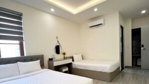 Quarto de hotel moderno com uma cama grande, uma cama menor, uma mesinha de cabeceira, um espelho e um ar condicionado.