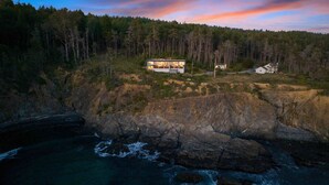 Una casa moderna con un'ampia terrazza, immersa in una foresta e affacciata su una costa rocciosa.