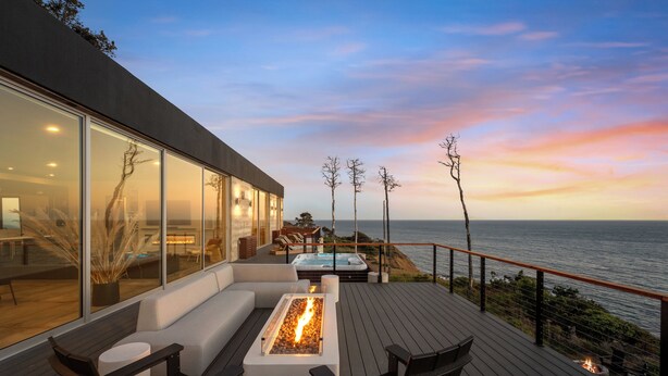 Una terrazza moderna con un focolare, posti a sedere e vista sull'oceano al tramonto.