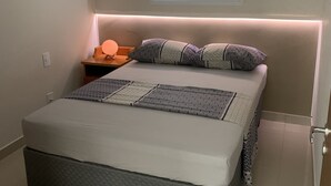 Une chambre à coucher comprenant un lit, des tables de chevet, une fenêtre avec des stores et une petite table de nuit avec une lampe.