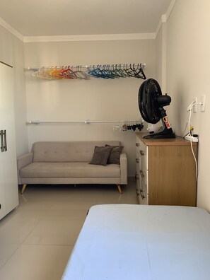 Una habitación pequeña y bien iluminada con sofá, ventilador, armario de madera y cama.