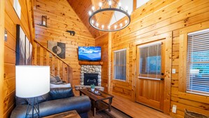 A cozy log cabin interior with a fireplace, a television, a sofa, and a dining table. - Spring Special! Hot Tub, Pools, Smart TV's, Wi-Fi, Arcade, Parkway! (Pigeon Forge)
