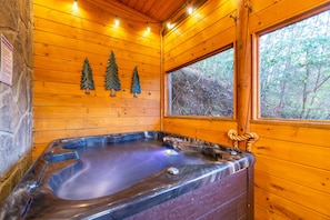 Een houten chalet met een jacuzzi, houten wanden en een raam met uitzicht op een bos.