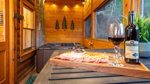 A wooden cabin interior with a wooden table displaying a charcuterie board, wine glasses, and a bottle of Mountain Valley Winery Cabernet Sauvignon. - Spring Special! Hot Tub, Pools, Smart TV's, Wi-Fi, Arcade, Parkway! (Pigeon Forge)