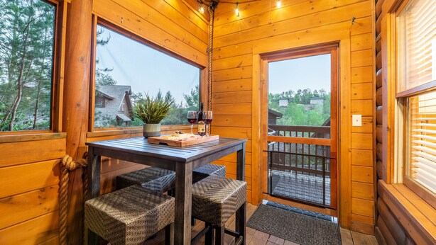 A wooden cabin interior with a dining table, chairs, and a balcony with a railing. - Spring Special! Hot Tub, Pools, Smart TV's, Wi-Fi, Arcade, Parkway! (Pigeon Forge)