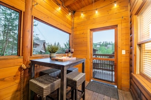 Een houten blokhut van binnen met een eettafel, stoelen en een balkon met een hekwerk.