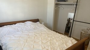 A bed with a white quilted cover, a wooden headboard, and a metal frame. - Main Street Crosby (Crosby)