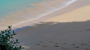 Une plage à l’eau turquoise et limpide, un rivage sablonneux et un phare qui se dessine à l’horizon.