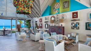 A beachside lounge with wicker furniture, a colorful wall with mirrors, and a view of the ocean.