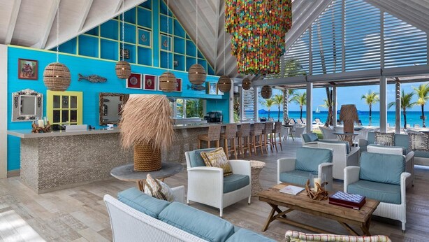 A spacious lounge area with a bar, wicker furniture, and a view of the ocean.