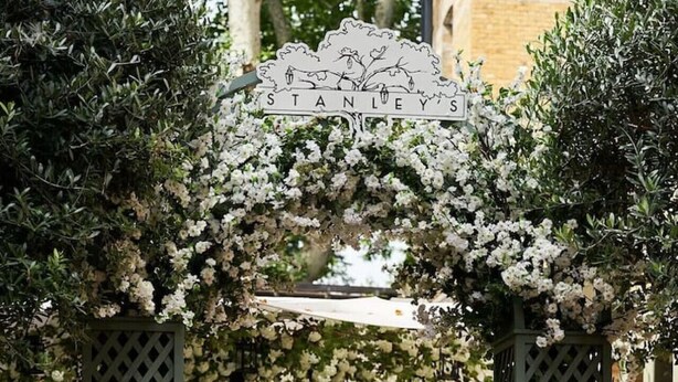 A garden entrance with a sign reading 'STANLEY'S,' a wooden gate, and a seating area with chairs. - A Chelsea Retreat - 2 BR with Garden and Parking (London)