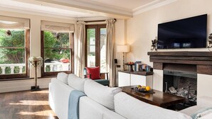 A living room with a sofa, a fireplace, a television, and large windows with curtains. - A Chelsea Retreat - 2 BR with Garden and Parking (London)