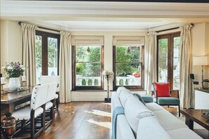 A spacious room with a large window, a sofa, a chair, and a table with a vase of flowers.