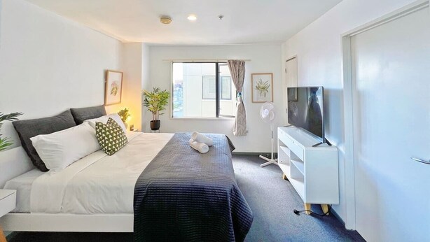 A hotel room with a bed, a TV, a desk, and a window. - Sky Tower View Studio in CBD (Auckland)