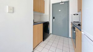 A compact kitchen with a dishwasher, a stove, and a door with a handle. - Sky Tower View Studio in CBD (Auckland)