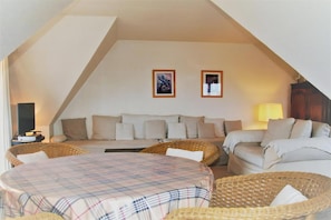 A cozy room with a sofa, a round table, and two wicker chairs.
