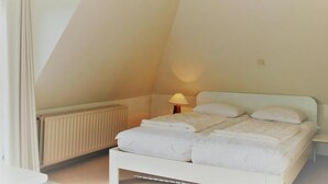 Quarto com cama branca, luminária de cabeceira e radiador.