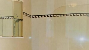 Casa de banho com lavatório branco, espelho, chuveiro com porta de vidro e chão em mosaico.