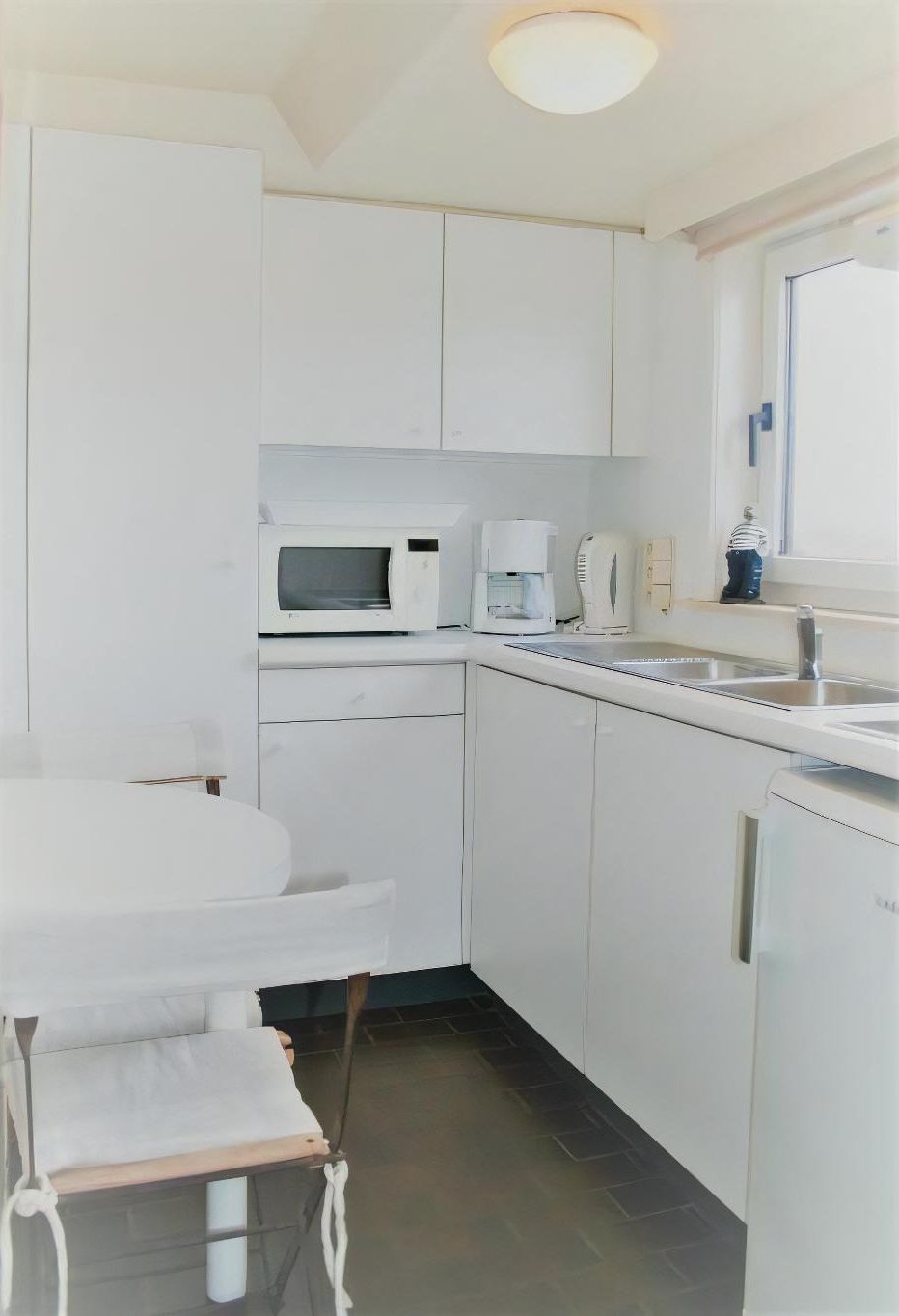 A compact kitchen with white cabinets, a microwave, a coffee maker, and a sink.