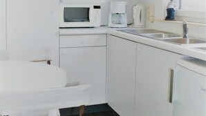 Uma cozinha compacta com armários brancos, micro-ondas, cafeteira e pia.