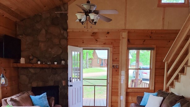Interior acogedor de una cabaña con chimenea de piedra, pisos de madera y una escalera.