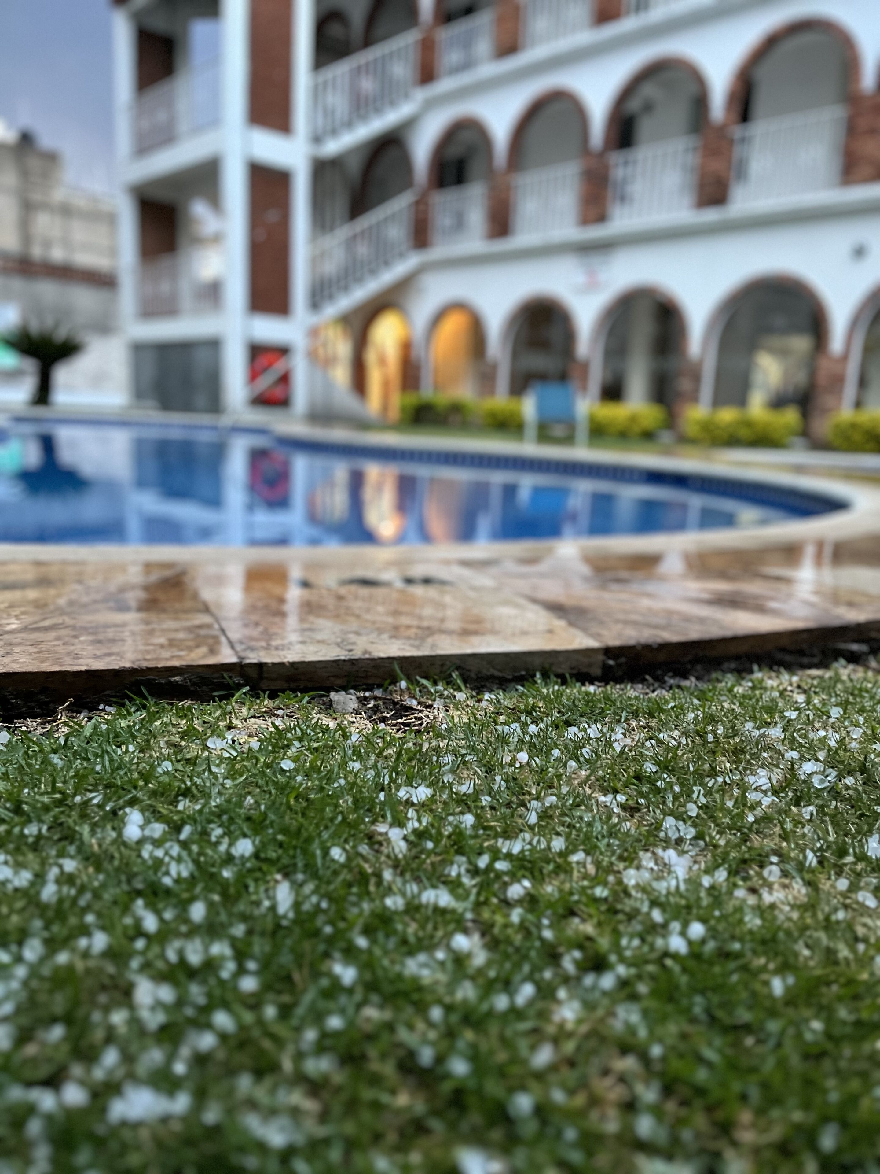 Ein Schwimmbad mit einer Holzdar Terrasse im Vordergrund und ein Gebäude mit Rundbogenfenstern im Hintergrund.